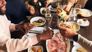 A mixed group of men and women sat at a restaurant table folled with drinks and charcuterie platteers as part of an early dining hospotality food strategy.