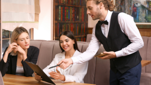 A formally dressed waiter explaining the menu to two young women in a reataurant. 