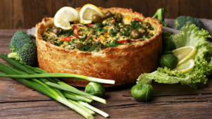 An open topped vegetable pie with broccoli, spring onions, sprouts, cabbage leaves, which is one of the top Christmas food trends in the UK, topped with green olives and lemon wedges. 