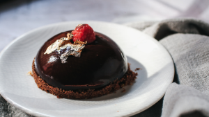 A dome-shaped rich chocolat mousse on a biscuit crumb base, topped with a raspberry.