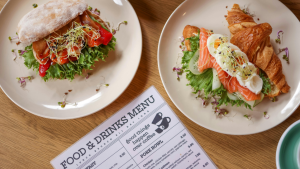 Two white plates with a salad pirra and a smoked salmon and egg croissant, next to a menu card.