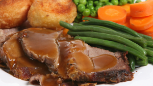 A plate of  roast lamb Easter Sunday lunch, with roast potatoes, carrot slices, peas, green beans and gravy.