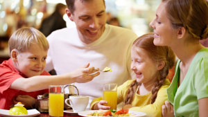 A young white mum, dad, and Gen Alpha son and daughter, smiling and dining at a restaurant table.