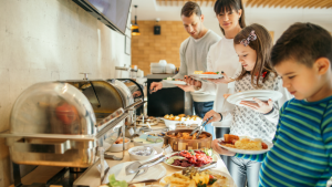 A young white mother, father, and Gen Alpha son and daughter filling their plates at a self-service buffet style restaurant.
