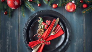 A green, red and gold Christmas place setting on a black plate and black table.