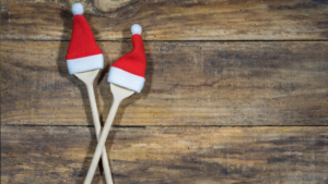 Two wooden spoons wearing mini Santa hats, on a wooden table
