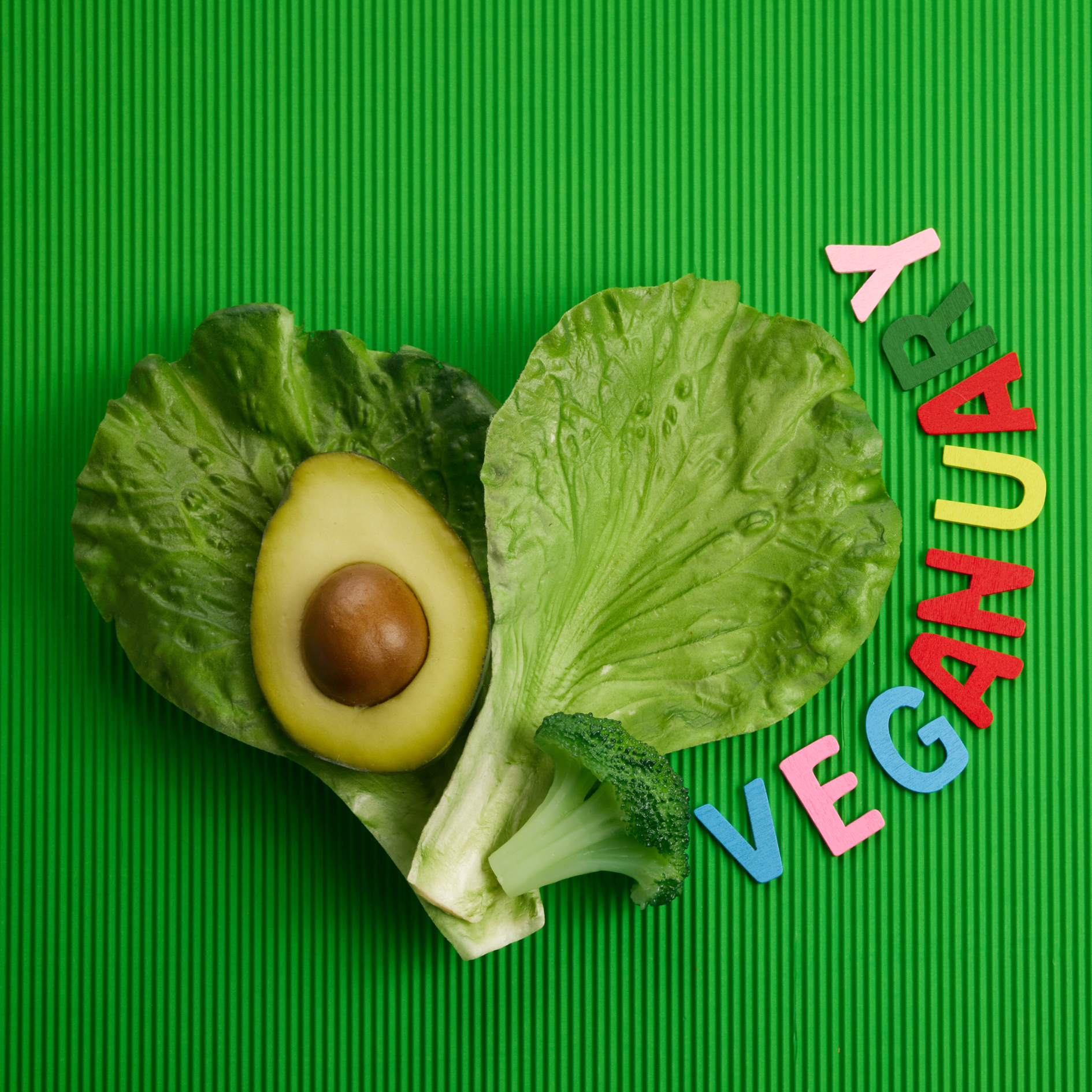 Lettuce leaves, a broccoli floret and half an avocado, next to coloured letters spelling VEGANUARY
