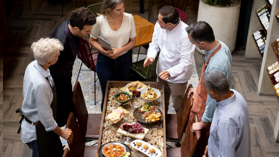 A group of chefs amd restaurant staff gathered around a table trying out new dishes as part of their seasonal menu strategy.