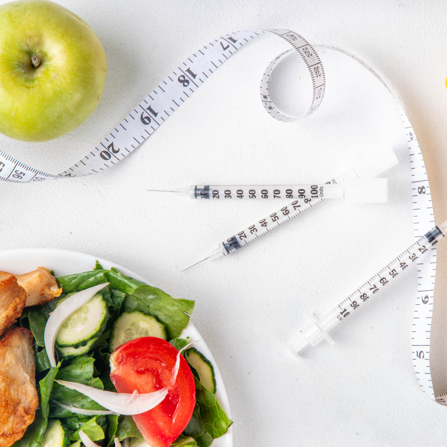 A plated chicken salad, a green apple, a tape measure, and three syringes, depictng the impact of weight loss drugs in the hospitality industry.