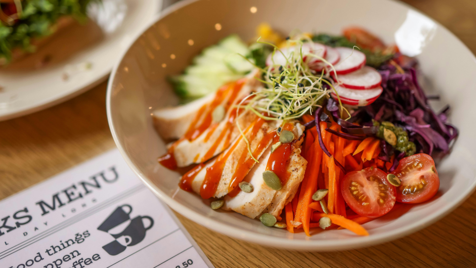 A chicken salad dish in a white bowl next to a menu card, for restaurant strategic food development.