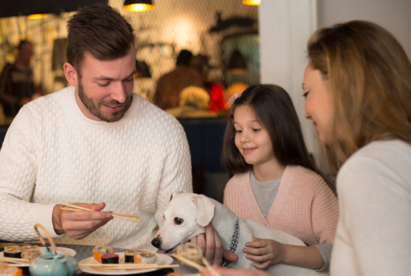 A young whie mother, father, Gen Alpha daughter and Jack Russell dog at a restaurant table, representing dictating the future of restaurant menus in the UK.