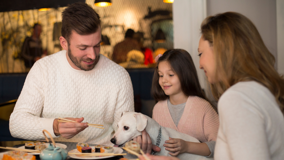 A young whie mother, father, Gen Alpha daughter and Jack Russell dog at a restaurant table, representing dictating the future of restaurant menus in the UK.