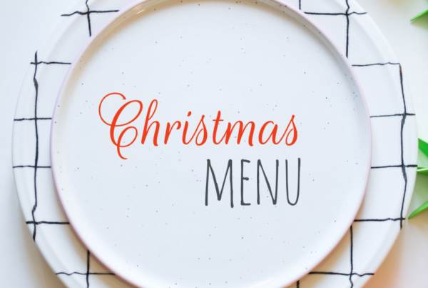 A white plate on a white table, decked with wintry foliage, with the words CHRISTMAS MENU